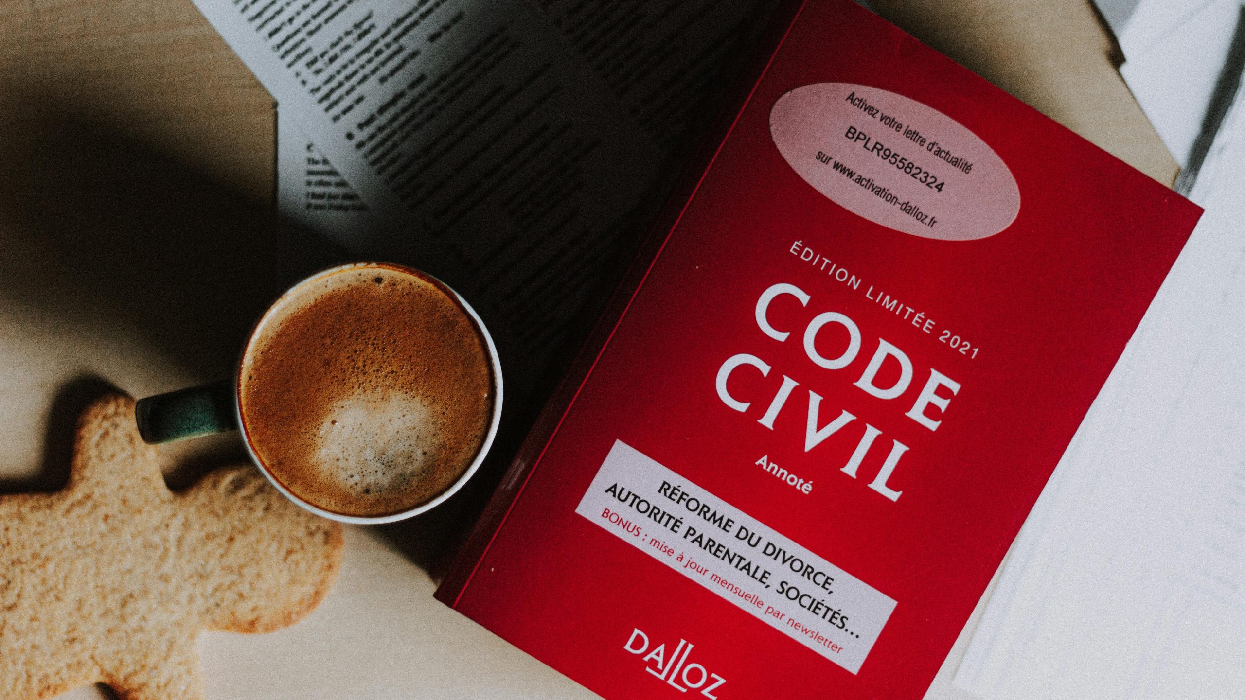 Cup of cappuccino and cookie placed near book on desk